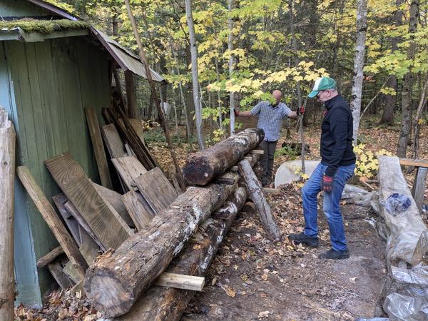 Ed and Jim at the restacked logs remaining from the repair of the kitchen wall.